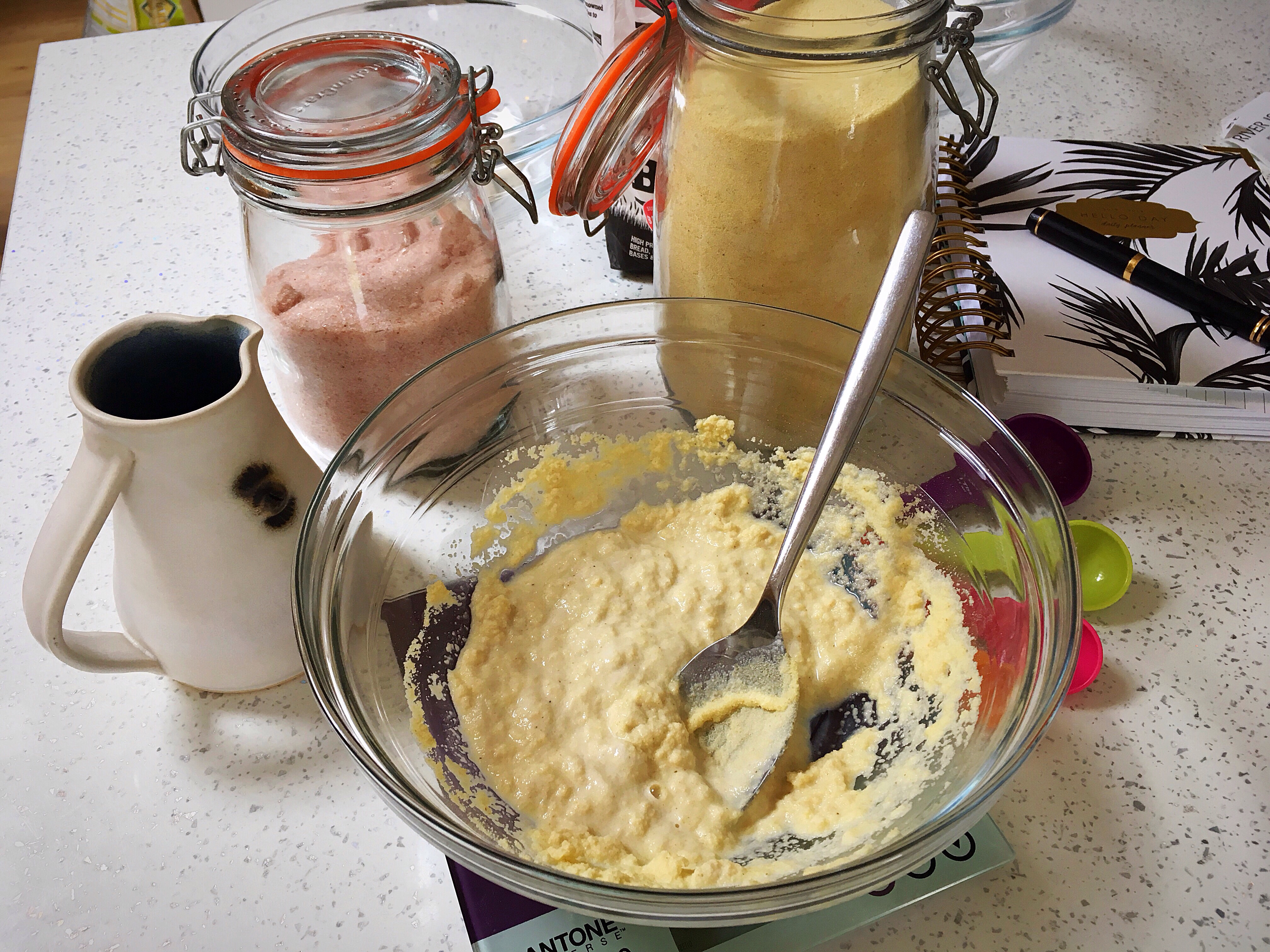 A bowl of food on the table with jars and spoons.