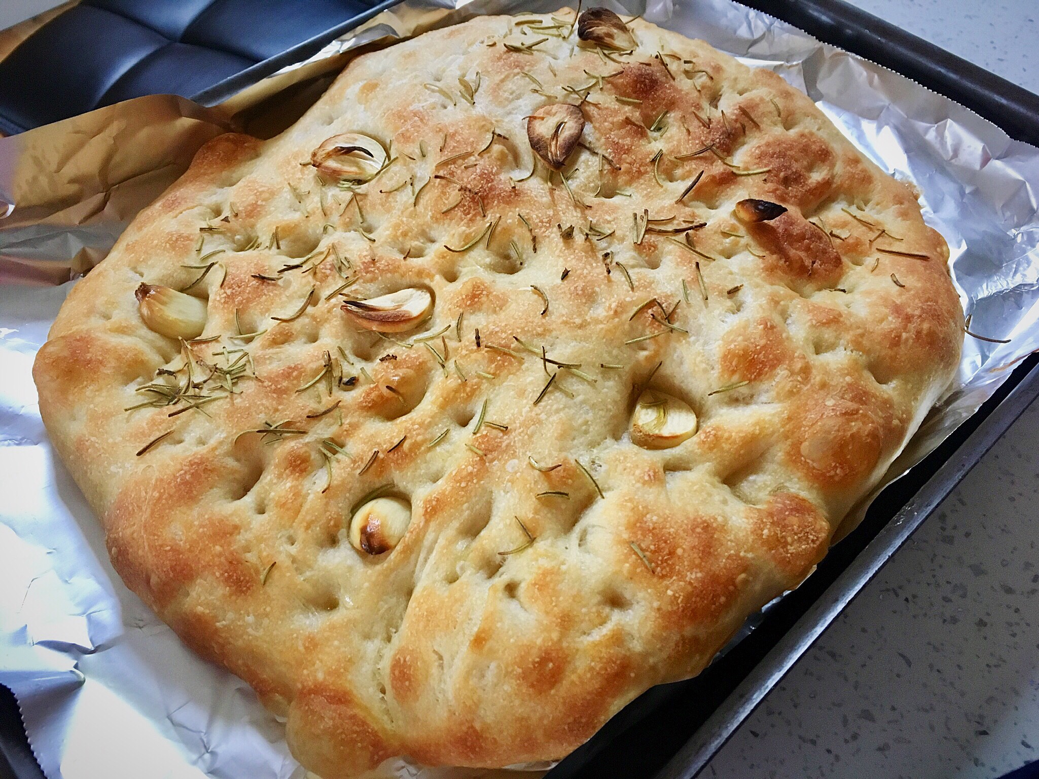 A square pizza with olives and herbs on it.