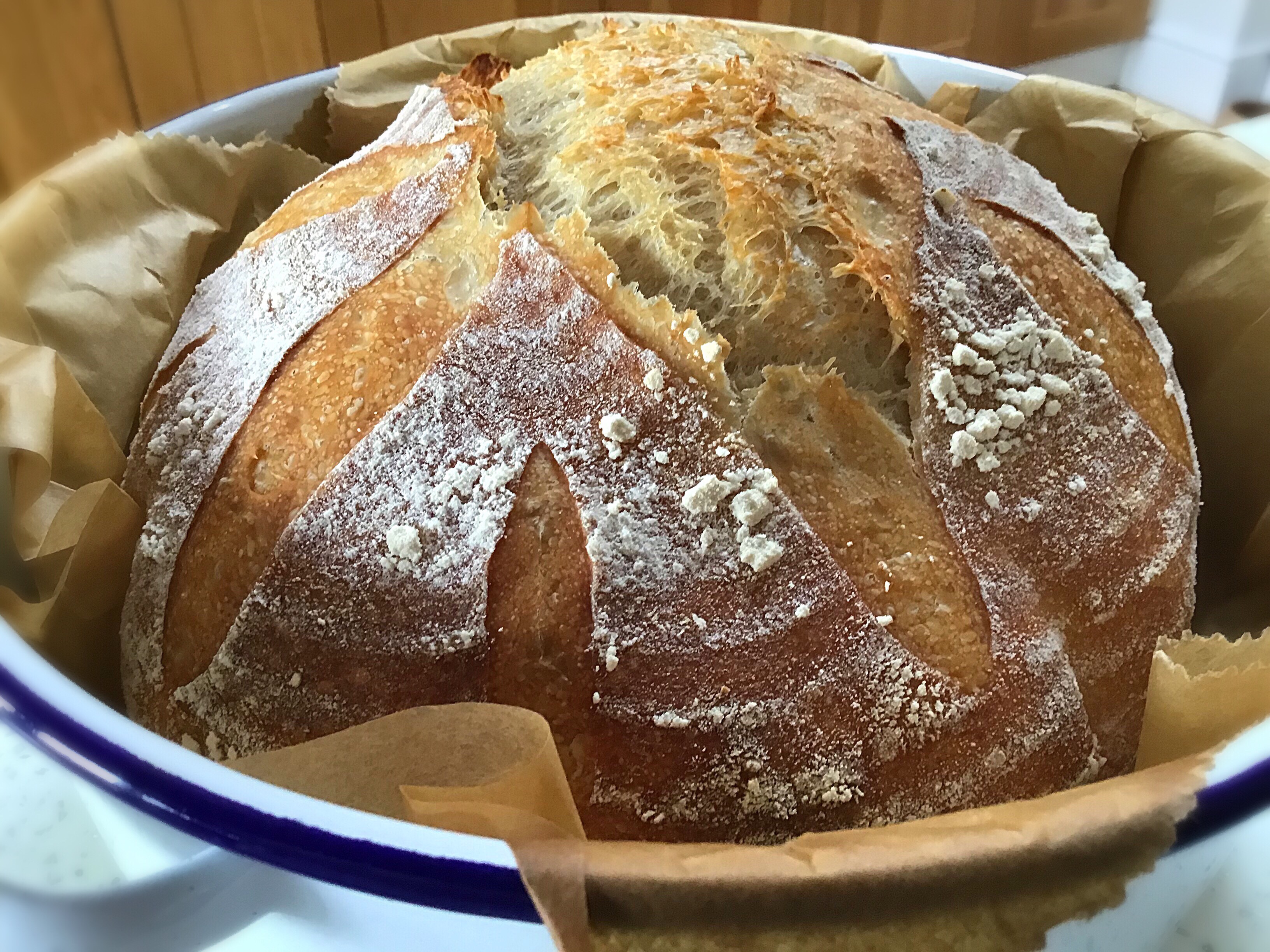 A loaf of bread in a bowl with a wooden spatula.