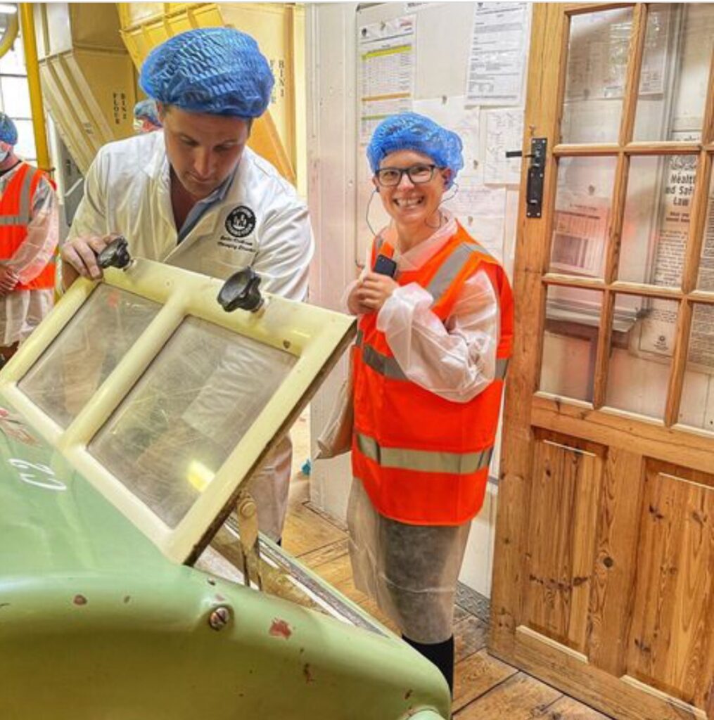 Two people in orange vests and blue hats standing next to a green machine.